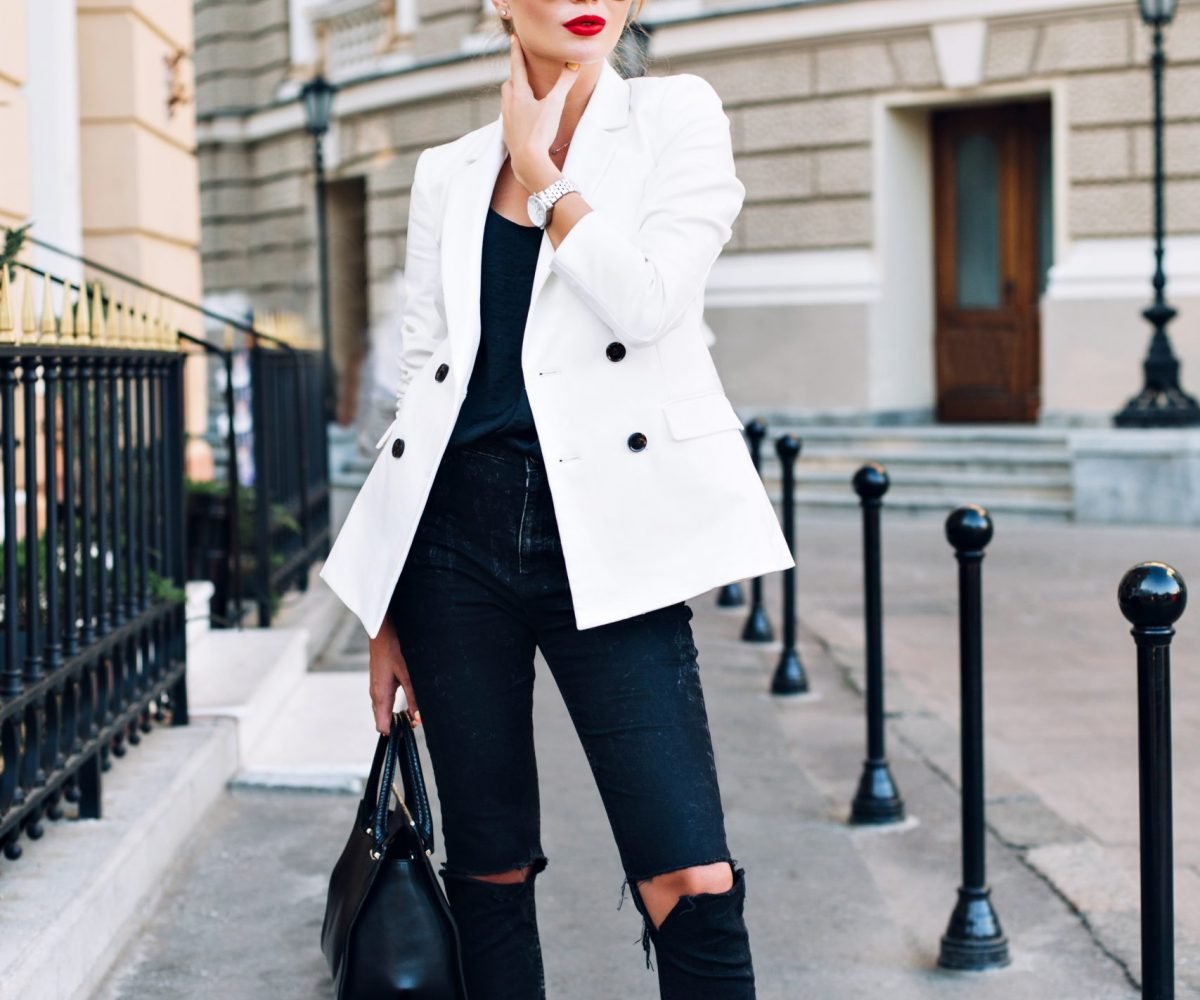 Fashion model is walking on street on heels. She wears sunglasses, ripped black jeans